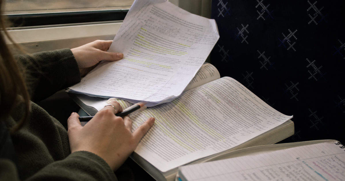 Hands on a train comparing a corrected printed draft with a highlighted academic article.