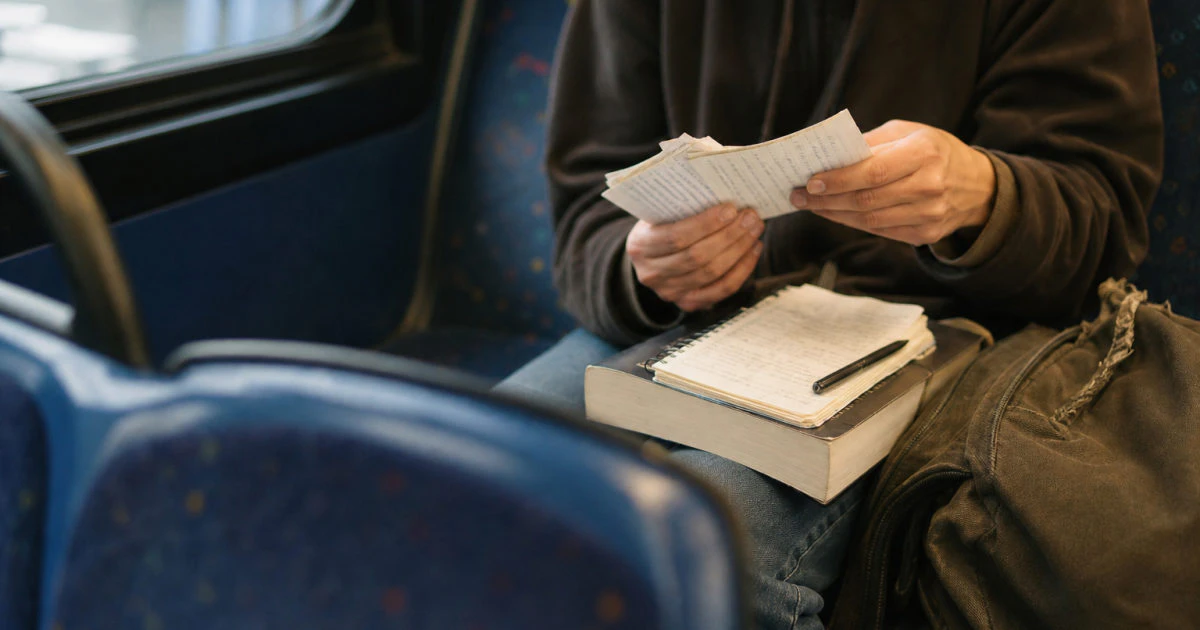 Student viewed from the shoulders down reviewing handwritten flashcards while seated on a bus.