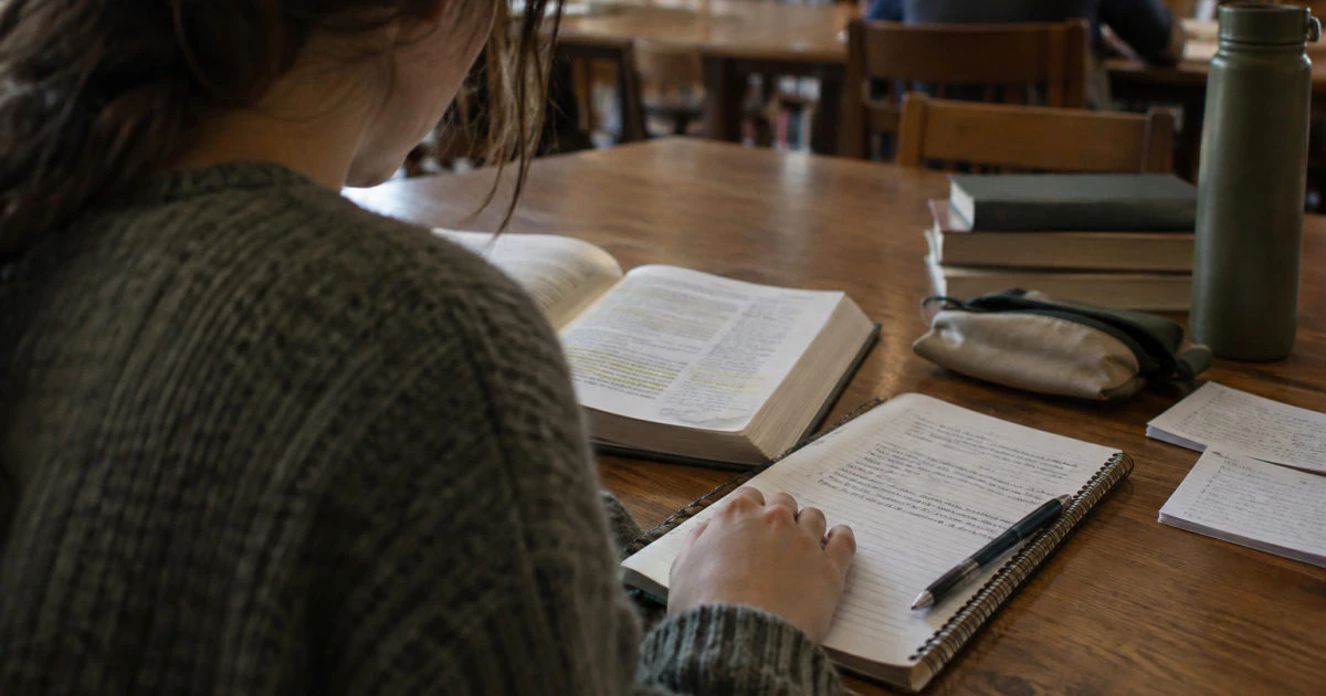 View over a student's shoulder of a highlighted textbook beside a notebook containing handwritten notes.